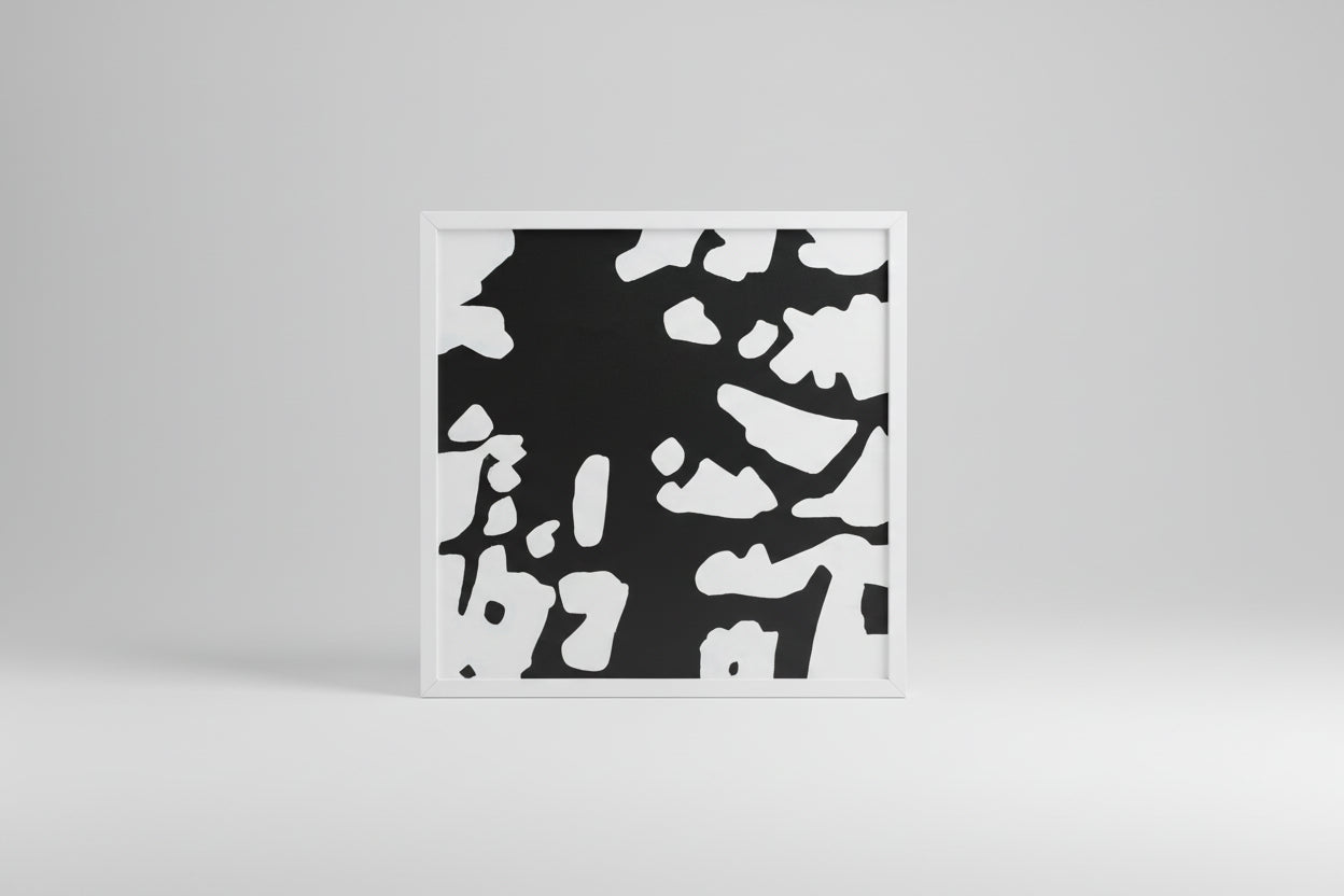 A framed abstract artwork featuring a black and white color pattern, displayed on a wooden surface with a custom white frame.