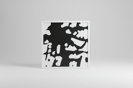 A framed abstract artwork featuring a black and white color pattern, displayed on a wooden surface with a custom white frame.