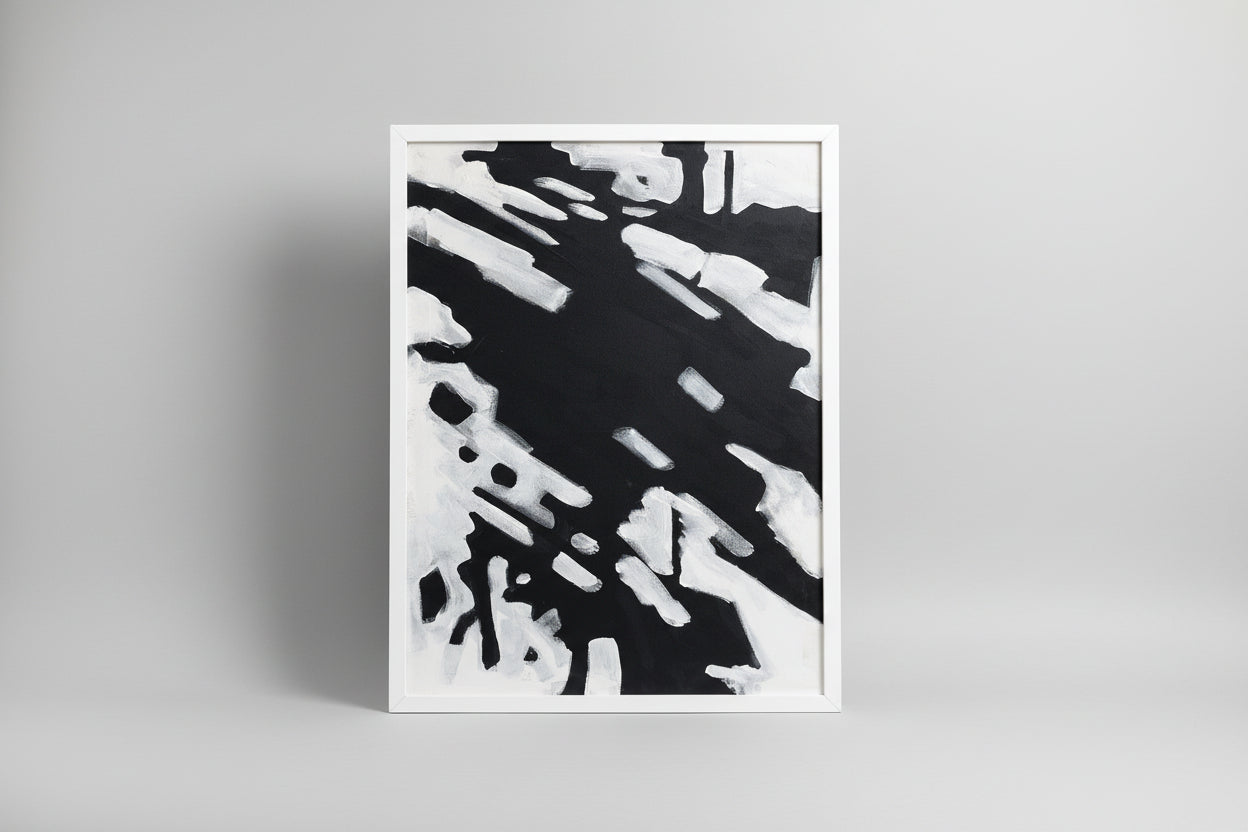 An abstract canvas painting featuring a custom white frame, displayed on a wooden surface with a sculptural object to the side in a home environment.