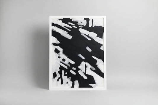 An abstract canvas painting featuring a custom white frame, displayed on a wooden surface with a sculptural object to the side in a home environment.
