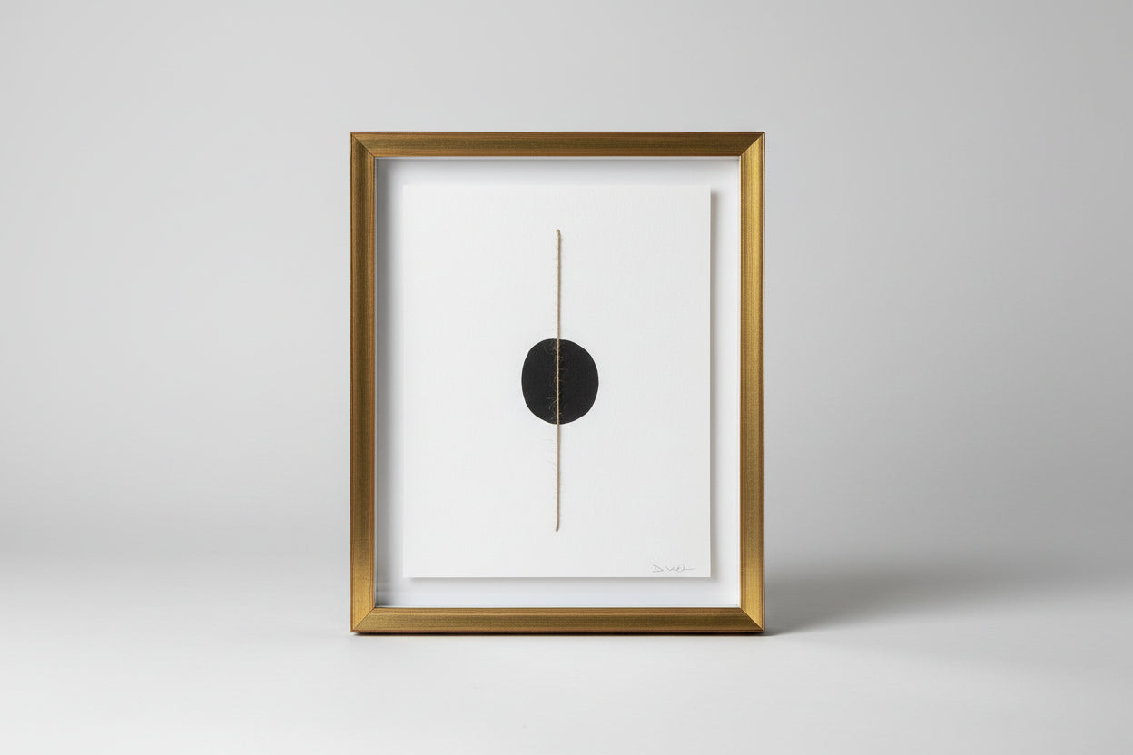 A framed artwork featuring a thin line drawing, displayed on a wooden surface with a blurred background.