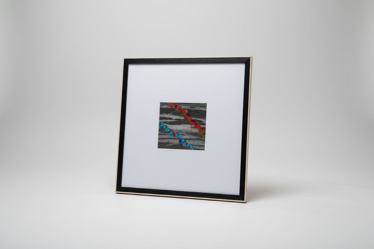 A framed mid-century abstract painting featuring geometric patterns with black, white, red, and blue colors, displayed on a wooden surface with a sculpture in the background.