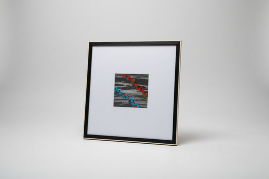 A framed mid-century abstract painting featuring geometric patterns with black, white, red, and blue colors, displayed on a wooden surface with a sculpture in the background.
