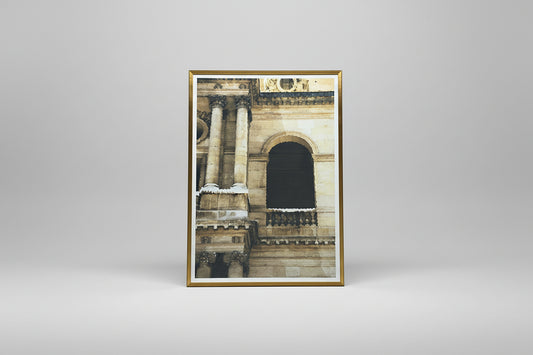 A framed lithograph depicting a architectural facade, displayed on a table with a well-lit background.