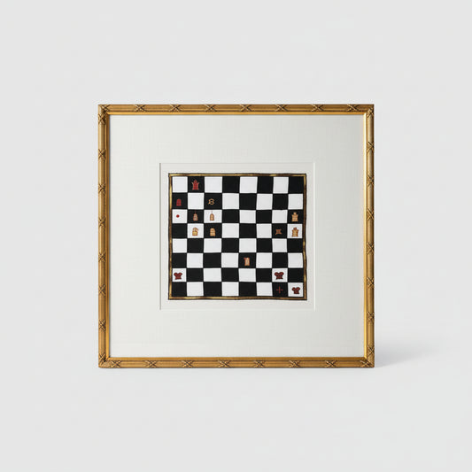 A framed decorative chess board with ornate gold frame, displayed on a wooden surface with a ball-shaped decorative item to the side.