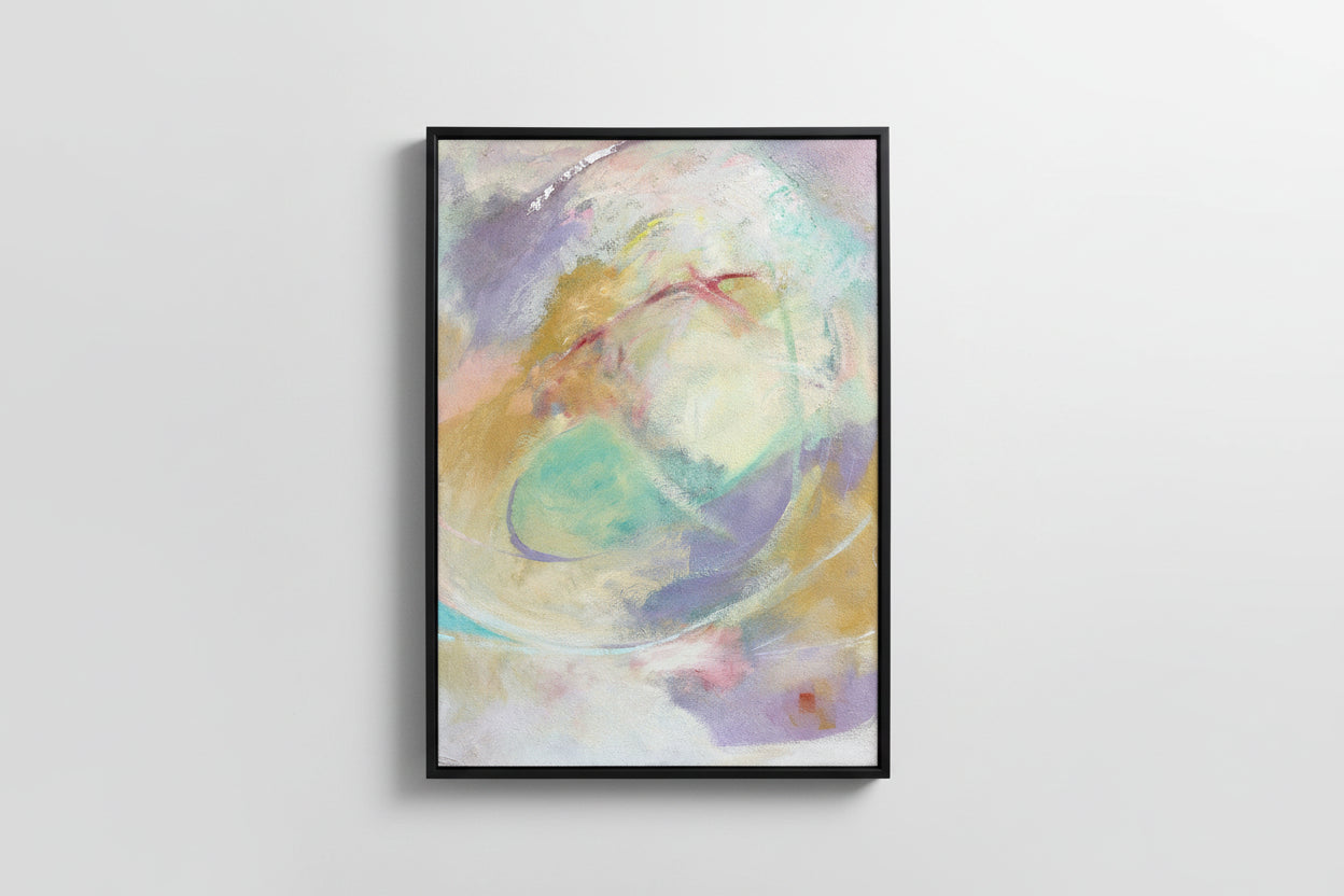 An abstract mixed media painting with a blend of pastel colors, framed in a black frame, displayed on a wooden surface.