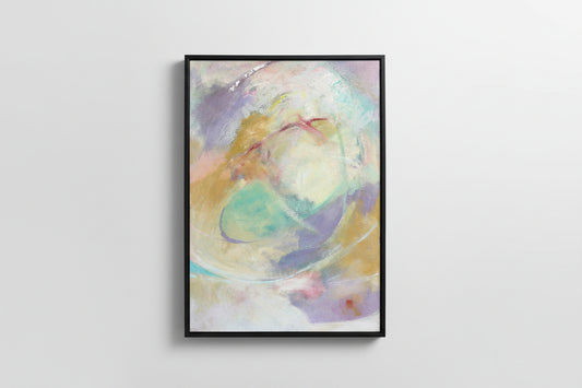 An abstract mixed media painting with a blend of pastel colors, framed in a black frame, displayed on a wooden surface.