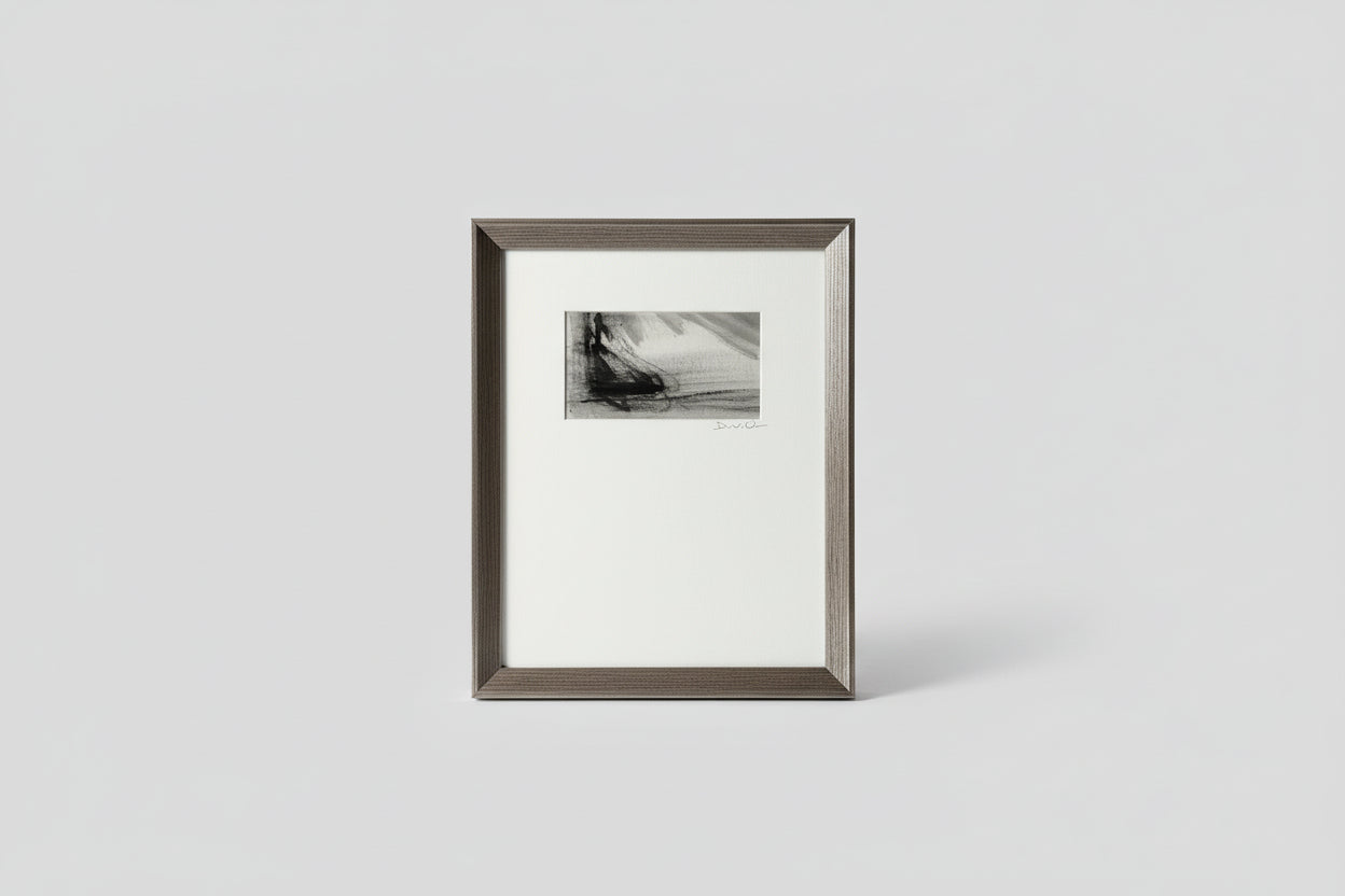A framed artwork featuring a monochrome scene with a boat on water, placed on a wooden surface with a plant in the background.