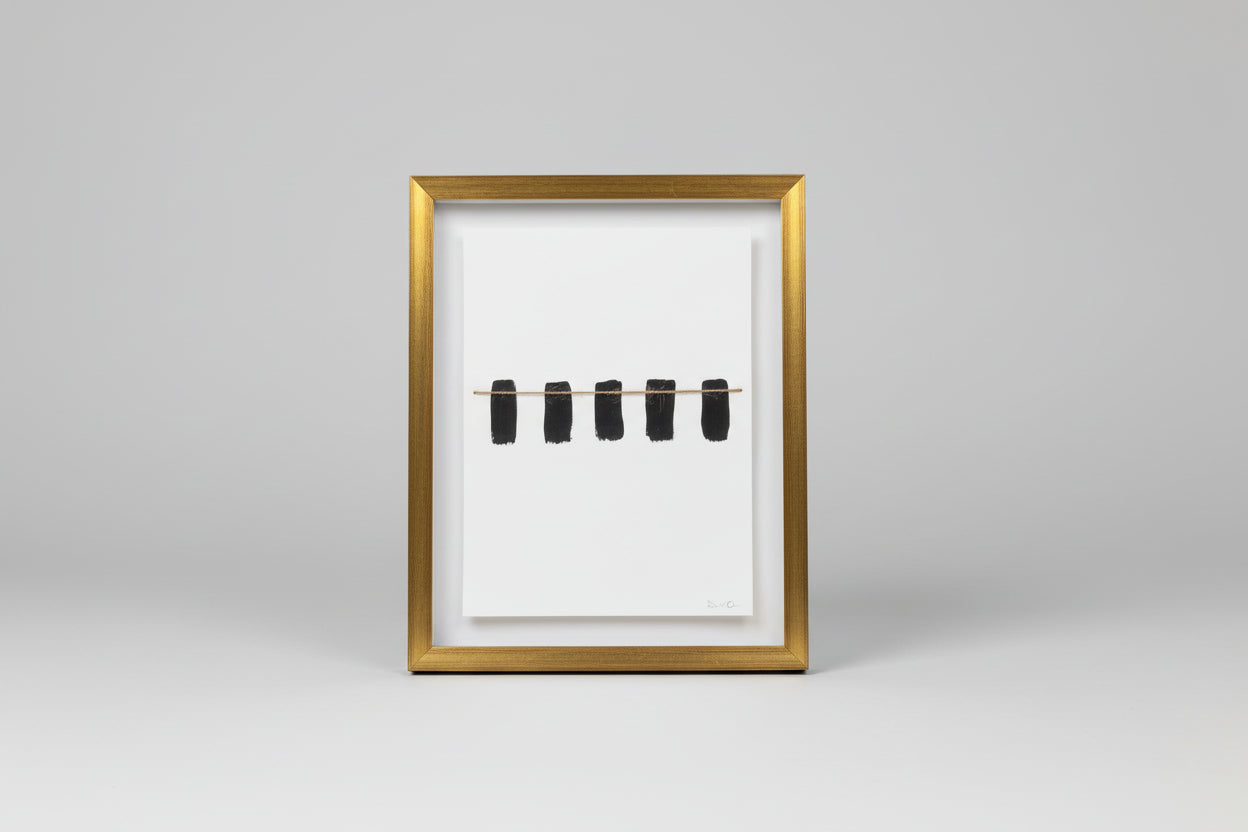 A framed artwork featuring a thin line segmented into four parts, displayed on a wooden surface with a black frame and a shadow falling on the wall.