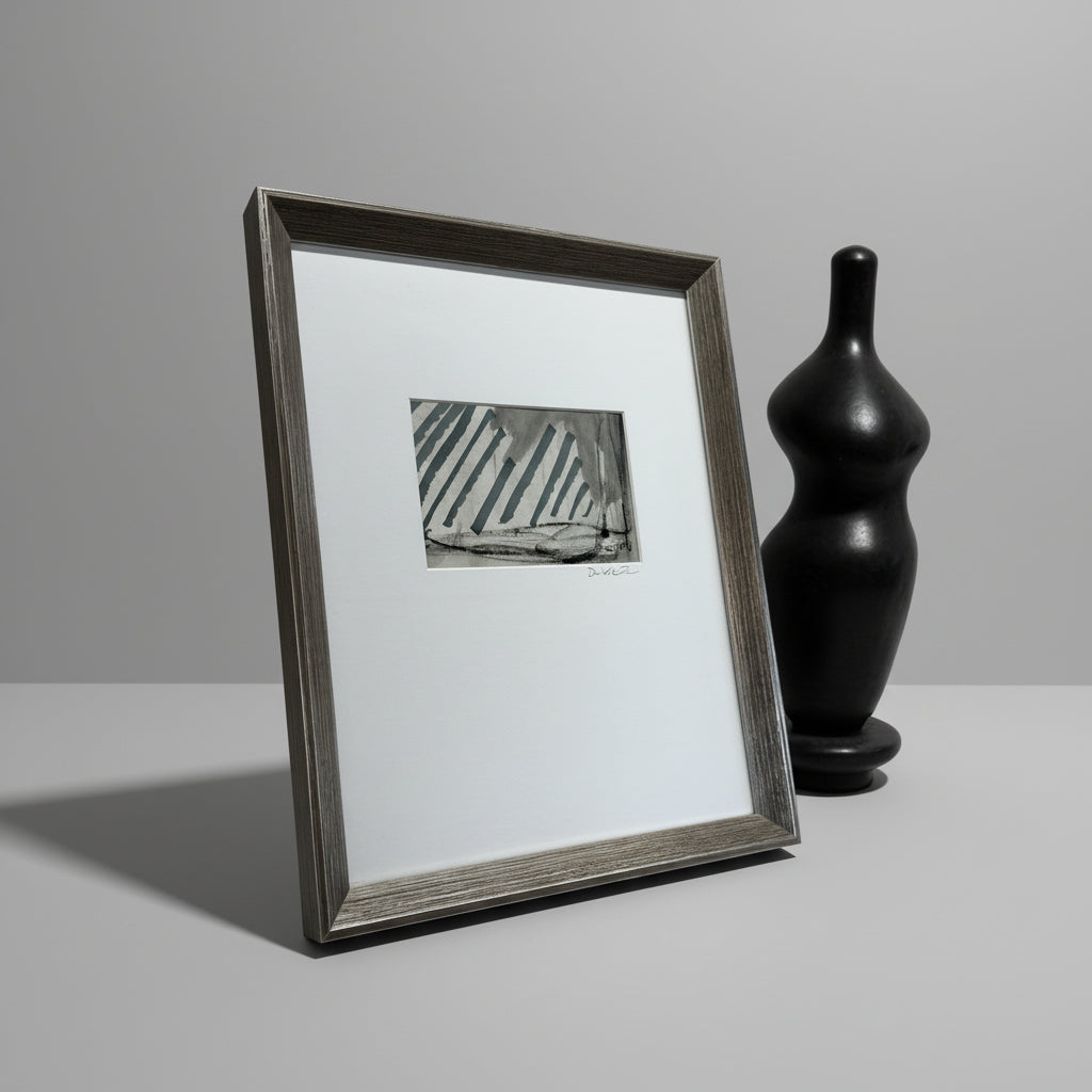 A framed artwork featuring geometric patterns in blue and white, placed on a wooden surface with a vase and sculpture in the background.