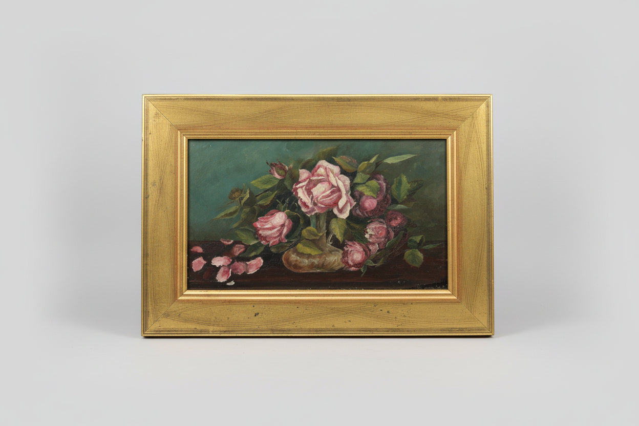 An oil painting of pink and red roses with green leaves, set within a gold-colored frame, displayed on a wooden surface.