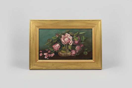 An oil painting of pink and red roses with green leaves, set within a gold-colored frame, displayed on a wooden surface.