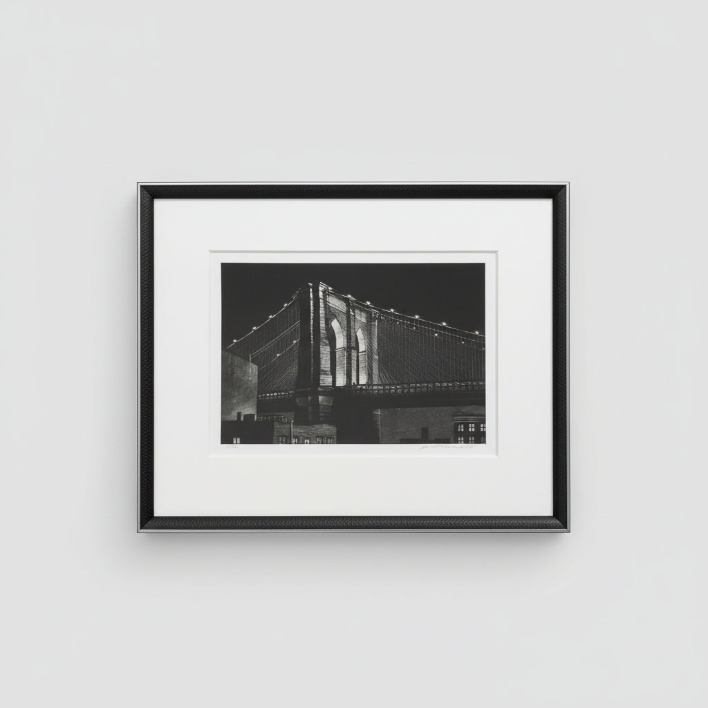 A framed and matted black and white photograph of the Brooklyn Bridge, displayed on a wooden surface.