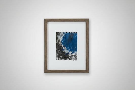A framed mixed media artwork featuring a blue and gray abstract pattern, displayed on a wooden surface with a custom-made frame.