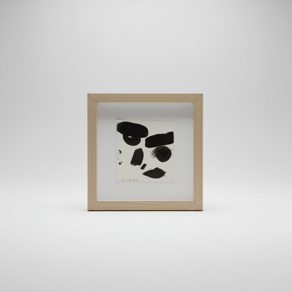 A framed ink portrait of a face on paper, displayed in a simple wooden frame, with the artist's signature visible on the artwork.