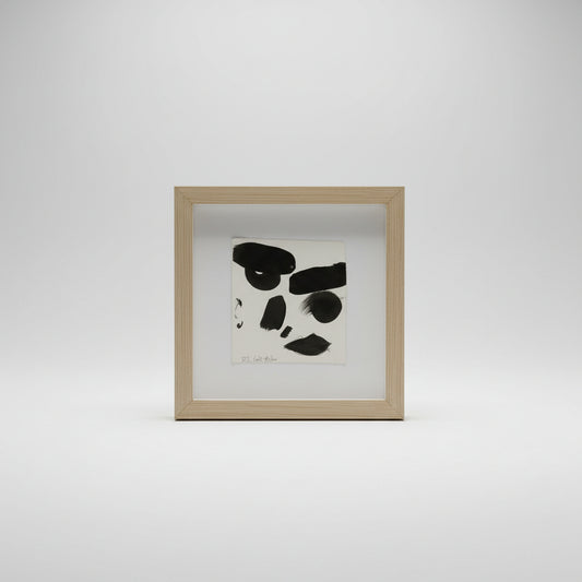 A framed ink portrait of a face on paper, displayed in a simple wooden frame, with the artist's signature visible on the artwork.
