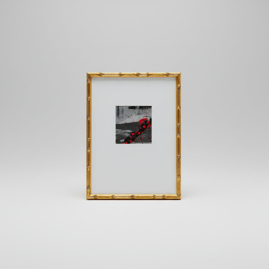 A gold bamboo frame around a abstract painting displayed on a wooden surface.