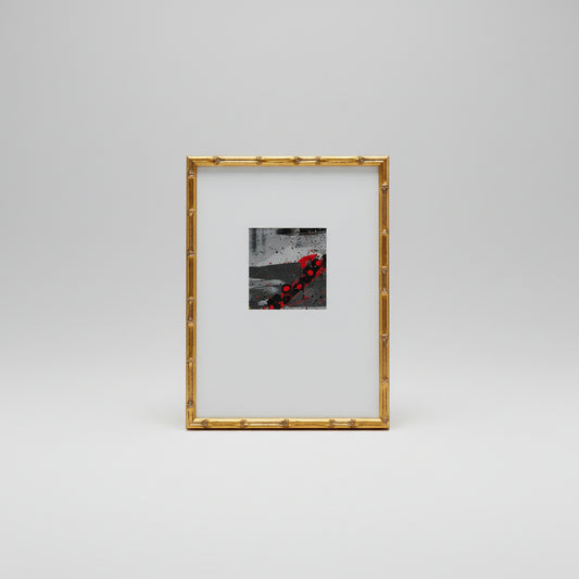 A gold bamboo frame around a abstract painting displayed on a wooden surface.