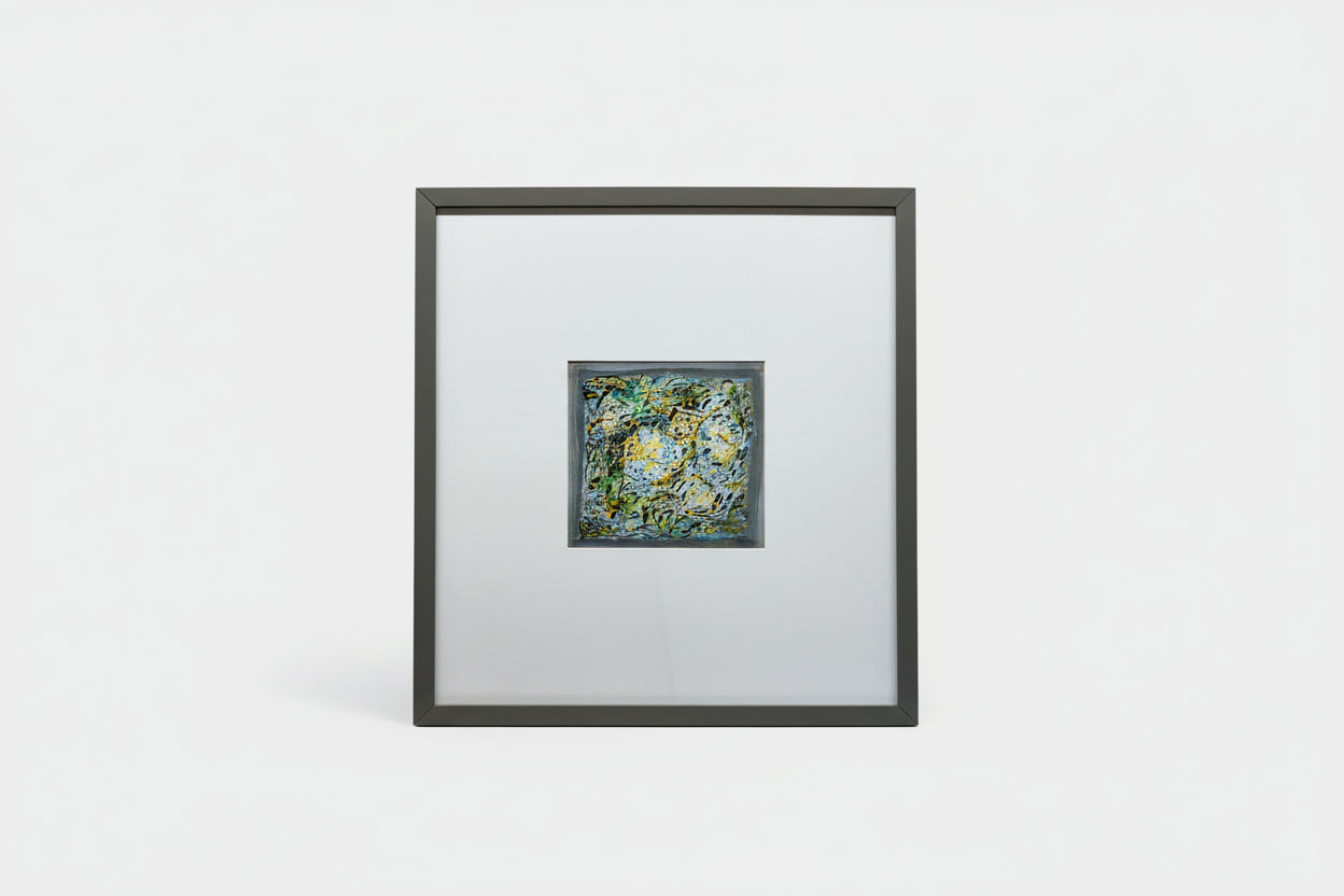 A custom framed abstract artwork featuring a mix of blue and green colors, part of the Whimsy in Wonderland series, displayed on a wooden surface with a black frame.