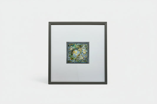 A custom framed abstract artwork featuring a mix of blue and green colors, part of the Whimsy in Wonderland series, displayed on a wooden surface with a black frame.