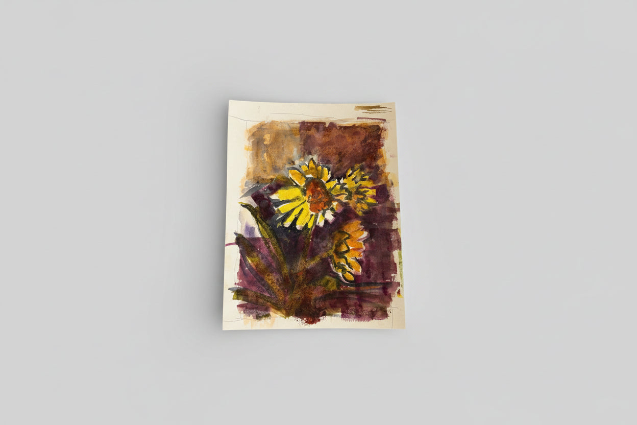 A framed mixed media artwork featuring a vibrant sunflower on a beige background, displayed on a wall above a counter with green moss.