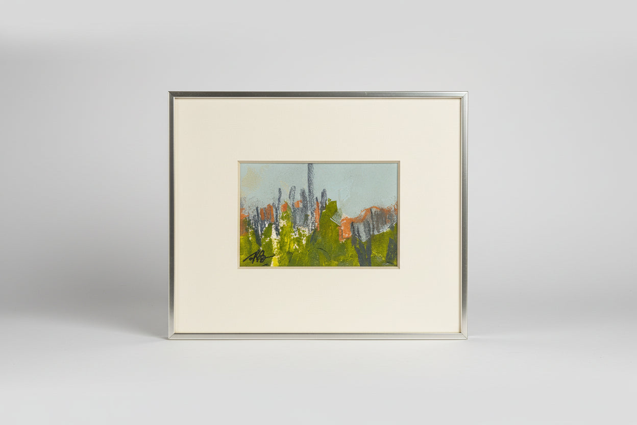 A framed mixed media artwork featuring a landscape with trees and buildings, displayed on a mantelpiece in a home setting.