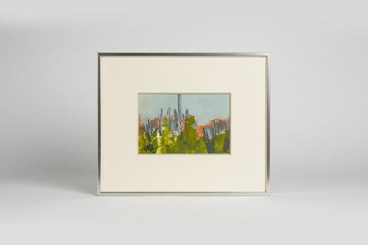 A framed mixed media artwork featuring a landscape with trees and buildings, displayed on a mantelpiece in a home setting.