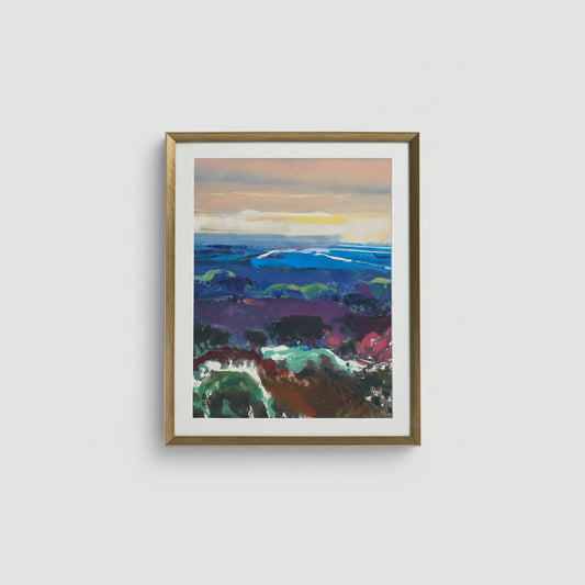 A framed mono print of a vibrant landscape view hanging on a wall, with a white frame and visible brushstrokes.