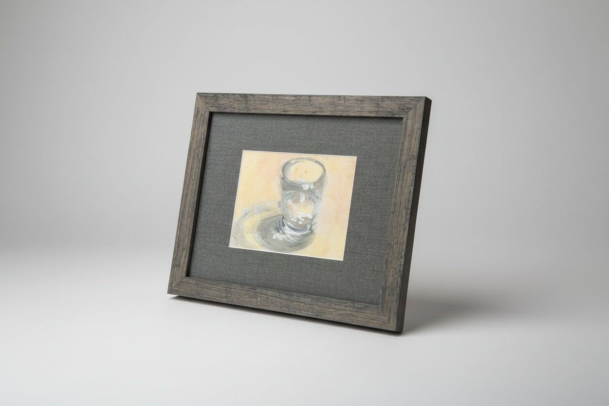 A framed water glass painting displayed on a stone surface with a window in the background.