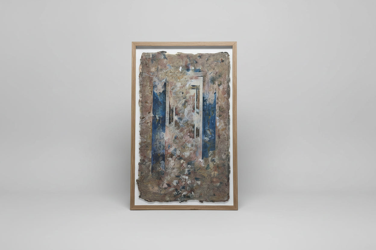 A framed paper carving art piece displayed on a wall, with natural elements visible through the artwork.