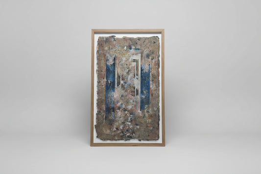 A framed paper carving art piece displayed on a wall, with natural elements visible through the artwork.