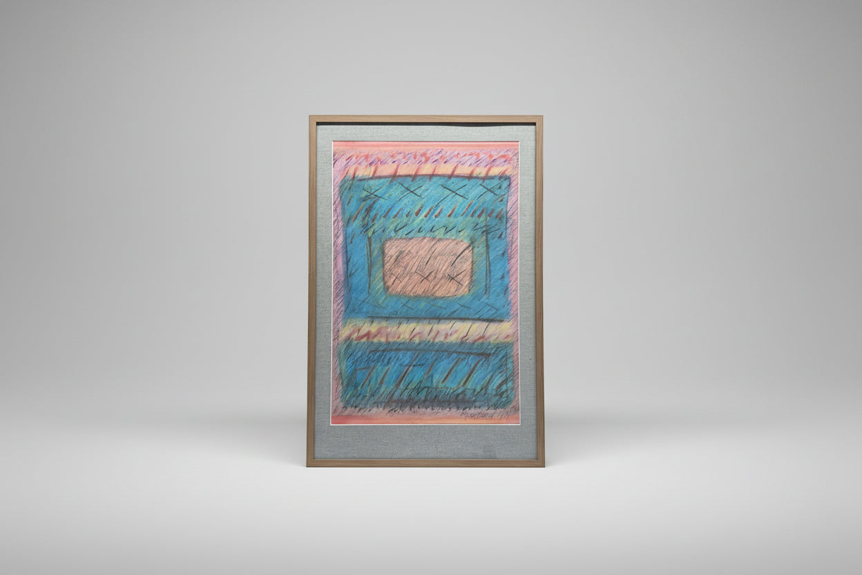 A framed mixed media artwork by Denise Freda, featuring geometric patterns with pink, blue, green, and beige colors, displayed on a table beside a plant.