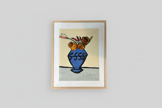 A framed painting of a blue vase containing multicolored flowers, displayed on a wall with natural lighting.