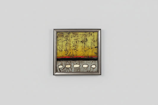 A framed painting depicting a serene pebble path, with a predominantly yellow and gray color palette, displayed on a wall.