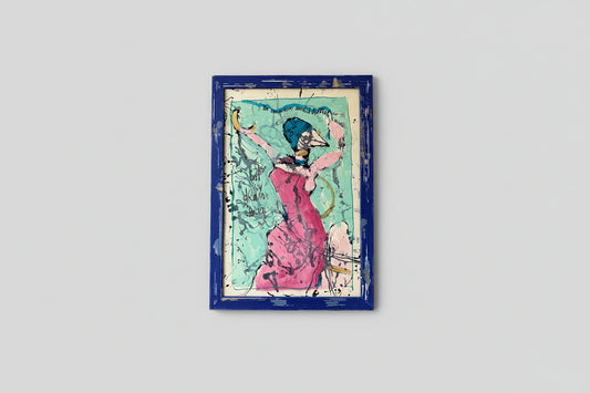 A mixed media artwork featuring a custom distressed frame, with a vibrant and colorful depiction of a female figure in a dramatic pose, hung on a wall above a wooden table in a well-lit room.