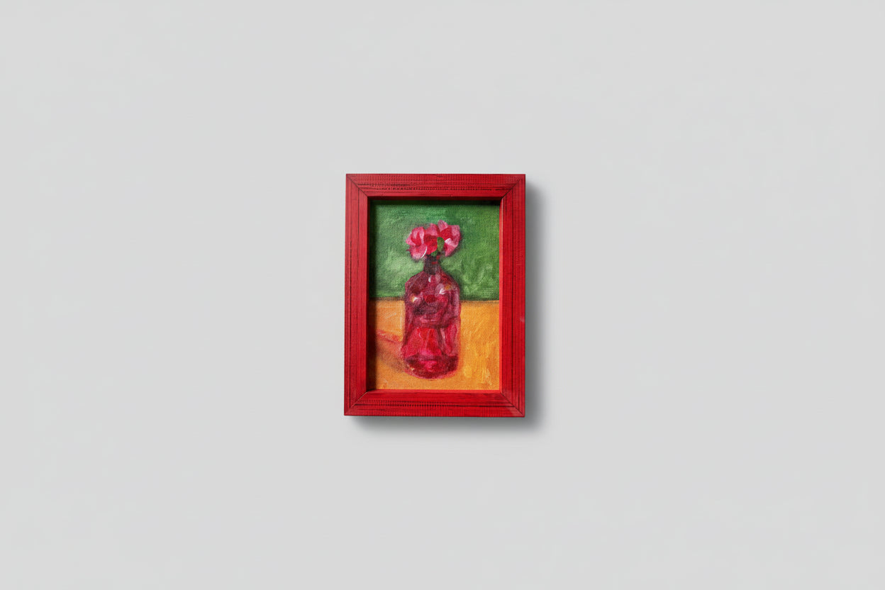 A painting depicting a red vase with petals, set in a red frame, displayed against a wall with some greenery in the foreground.