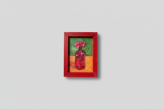 A painting depicting a red vase with petals, set in a red frame, displayed against a wall with some greenery in the foreground.