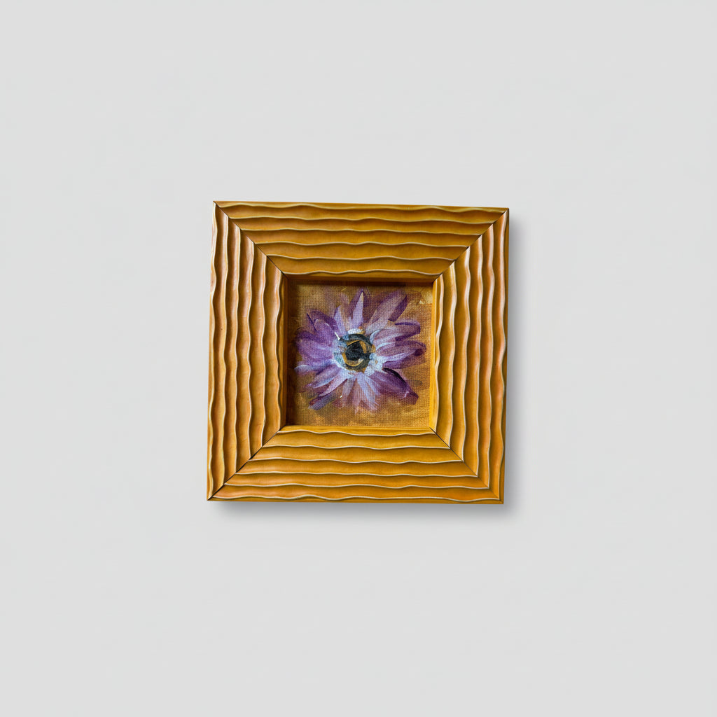 A painting of a daisy with a gold frame, displayed on a wall.