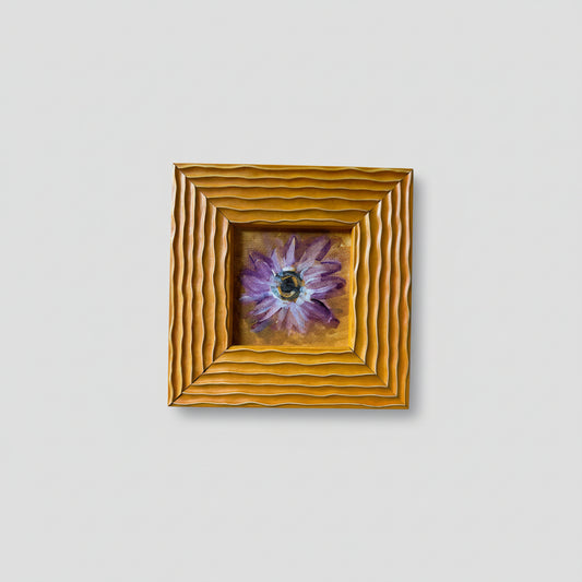 A painting of a daisy with a gold frame, displayed on a wall.