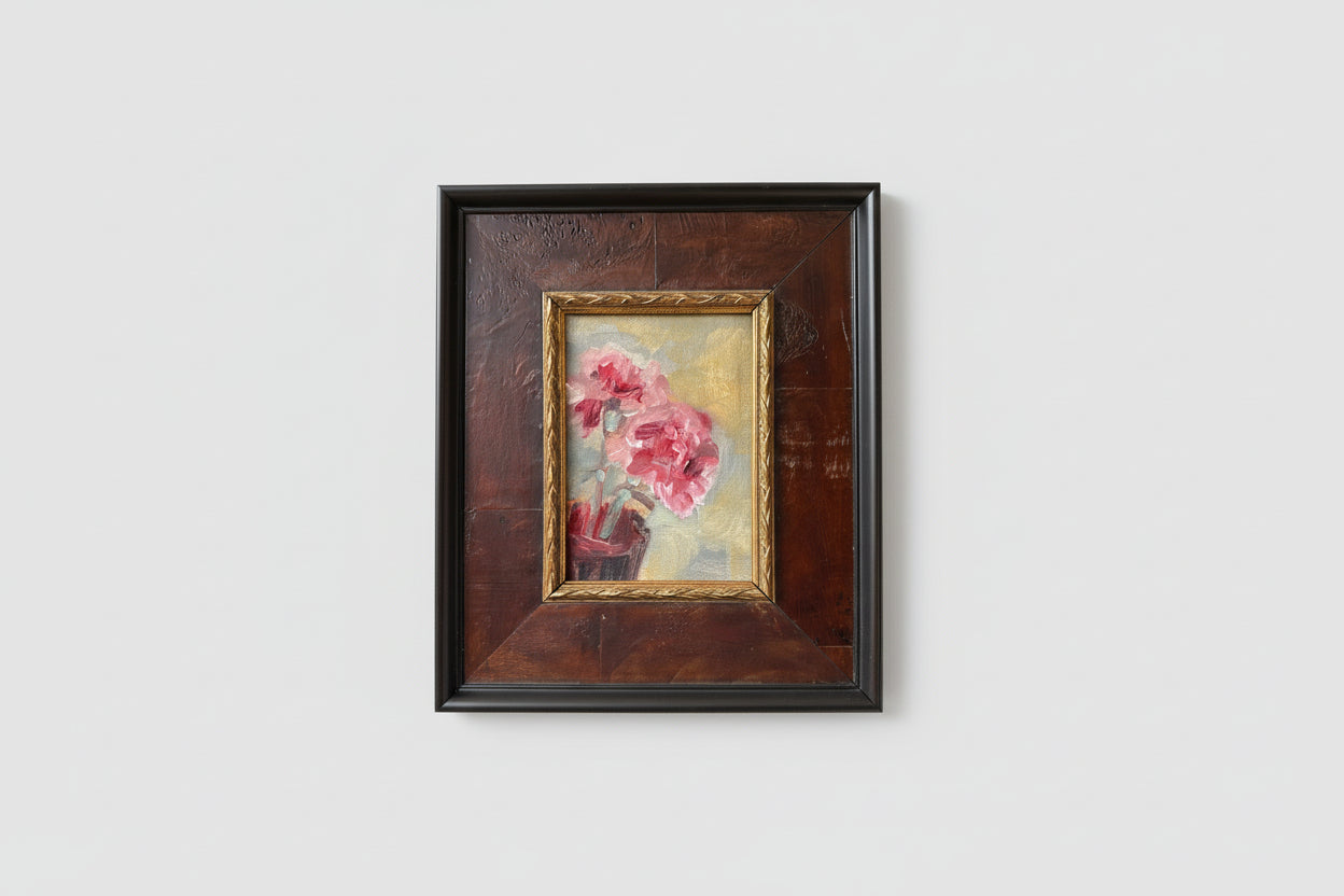 An oil painting of pink flowers on a board, encased in a burl wood frame, displayed on a wall.