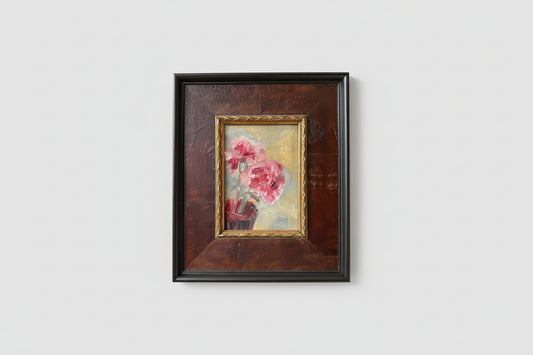 An oil painting of pink flowers on a board, encased in a burl wood frame, displayed on a wall.