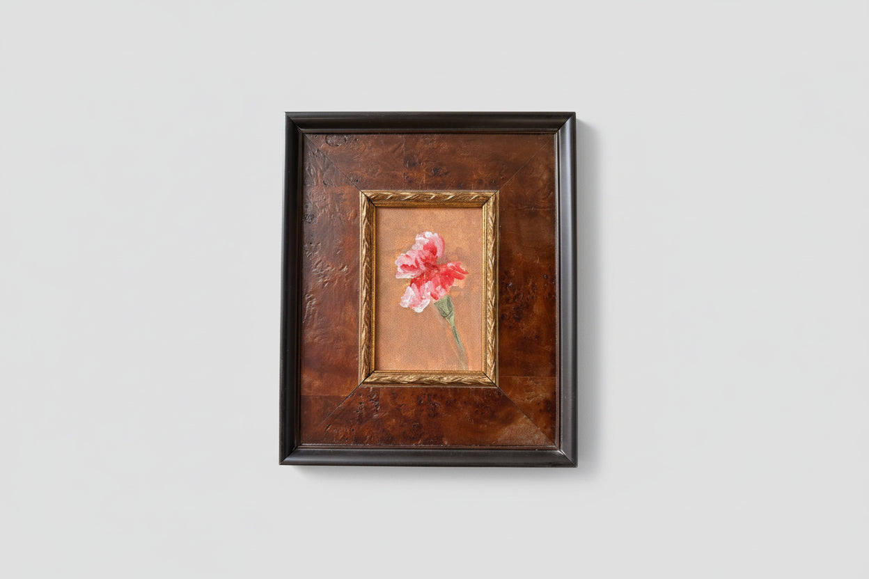 An oil painting of pink flowers on a board, framed in a burl wood frame, displayed on a wall.