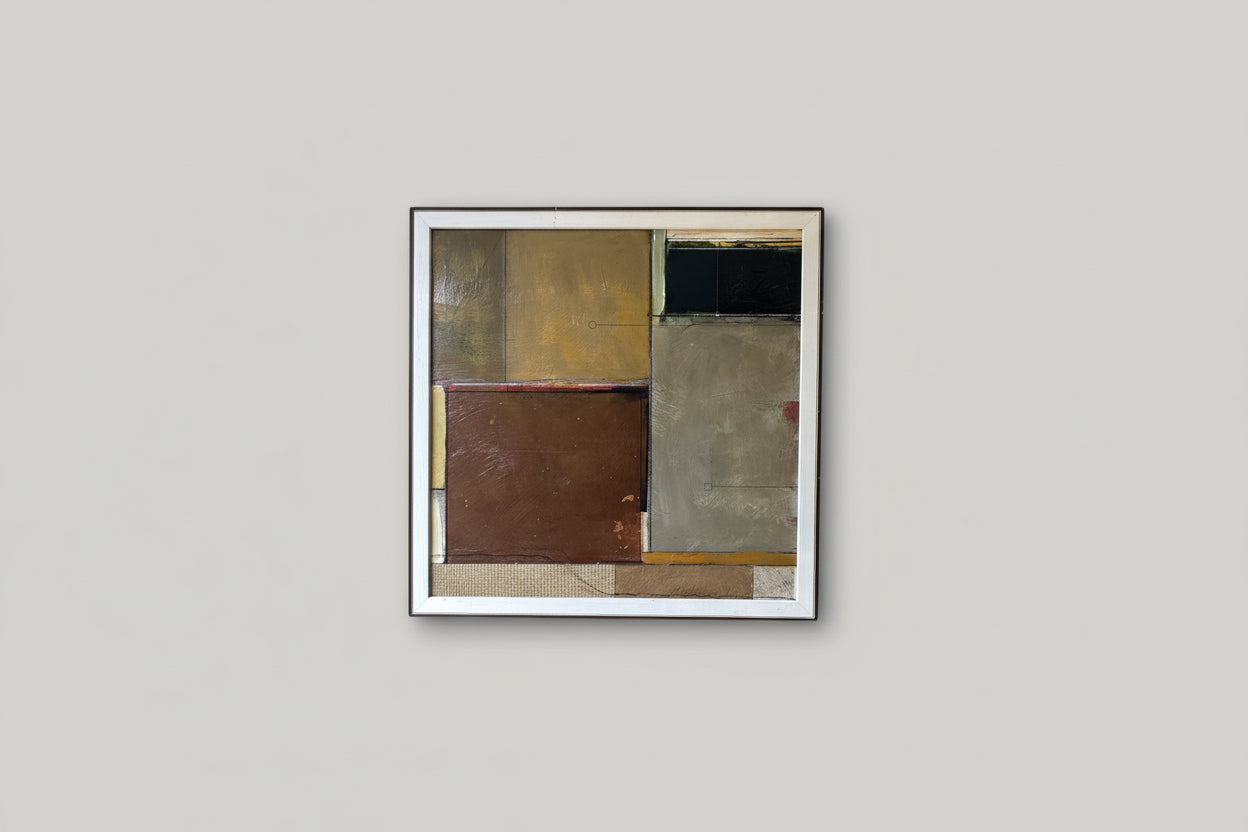 A geometric artwork piece framed in a square frame, hanging on a wall in a well-lit room with plant decor.