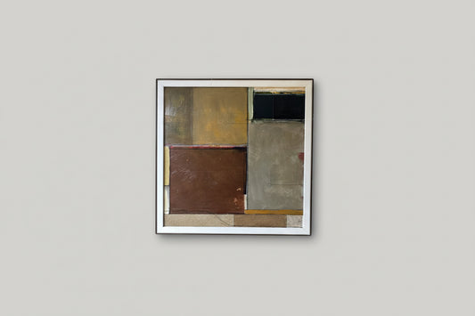 A geometric artwork piece framed in a square frame, hanging on a wall in a well-lit room with plant decor.