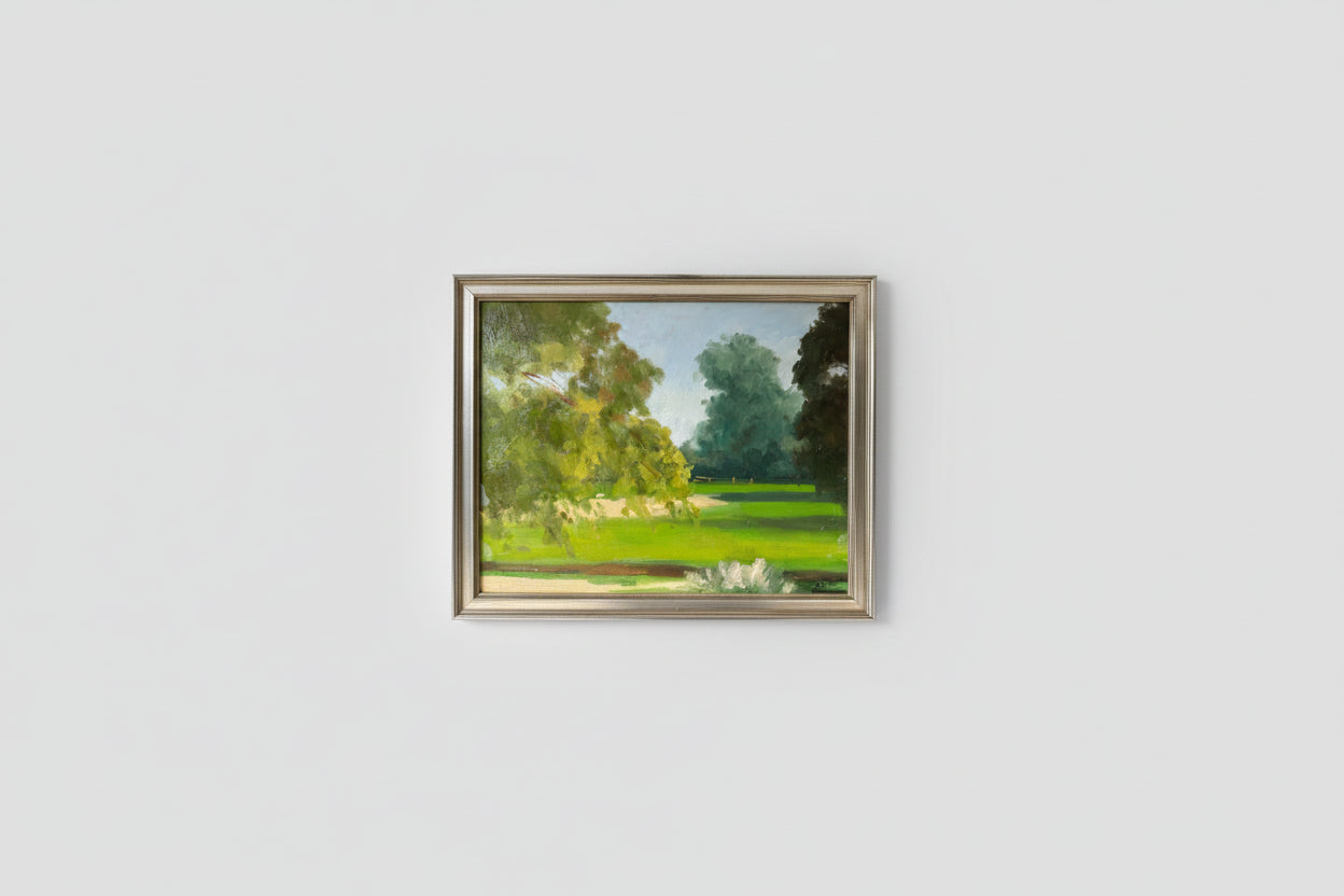 An oil on board artwork depicting a park scene, framed in a silver frame, displayed on a wall.