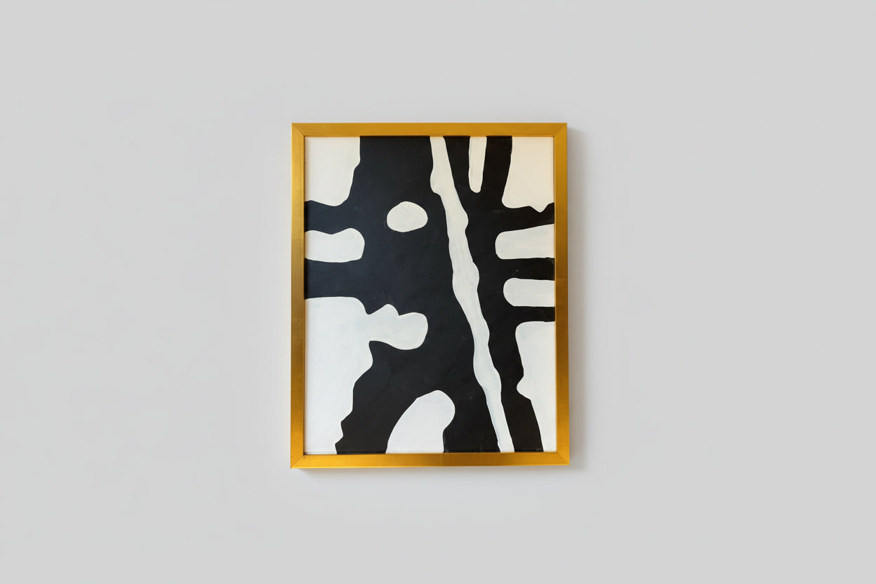 An abstract artwork with black and white colors and a custom gold frame, displayed on a wall.