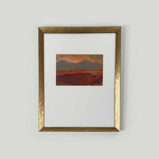 Framed painting of a landscape with warm colors on a white wall.